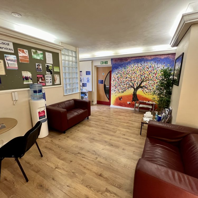 the inside of our Ware crisis cafe, which has sofas, a water machine, tables, chairs, posters, plants, and colourful artwork