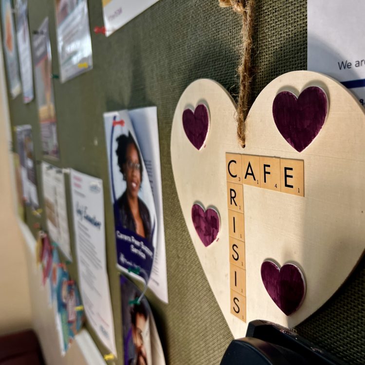 the photo shows one of the walls inside the Ware crisis cafe, featuring a wooden heart decoration with hearts and the words crisis cafe in scrabble style