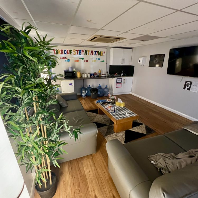 the photo shows the inside of our Stevenage Crisis Cafe, including two sofas, a table, a plant, a television and a kitchen area