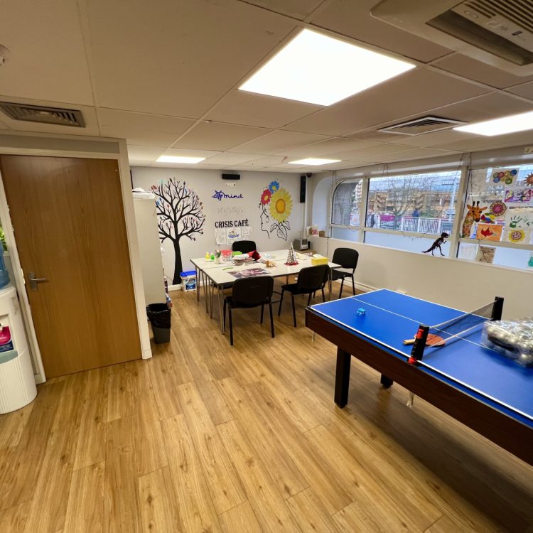 the photo shows the inside of our Stevenage Crisis Cafe, including a table football, chairs and tables, a water fountain and artwork on the walls