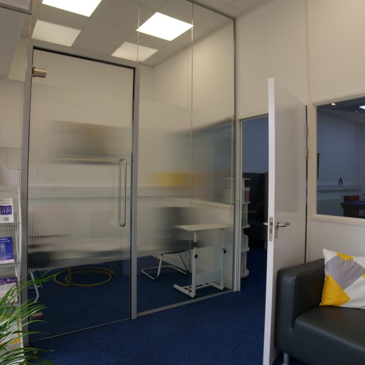 the photo shows an inside room from our Hatfield crisis cafe, including a sofa, a plant, leaflet stack, and private room with a glass door